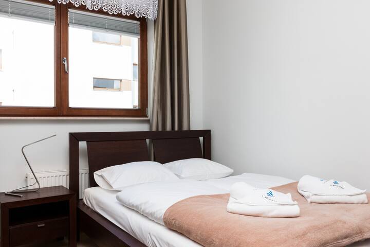 המיטה הכפולה עם כיסוי מיטה רך ומצעים לבנים מבטיחה שנת לילה שלווה בחדר שינה נעים.