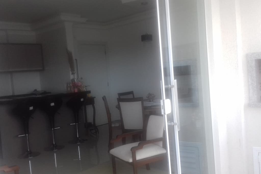 Cozinha; bancadas e banquetas; mesa de jantar e churrasqueira à direita