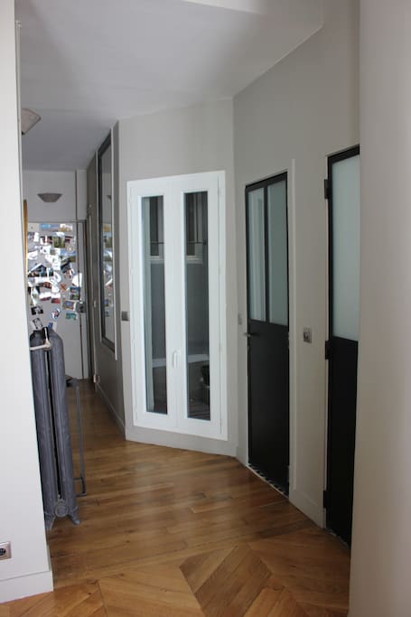 Porte d'entrée au fond et porte-fenêtre blanche du patio. A droite, la première porte noire : WC et la seconde : SDB