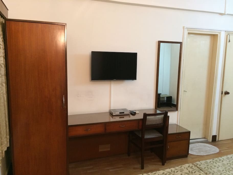 This shows a cupboard, TV, full length mirror, writing table/ laptop space and the door to the bathroom