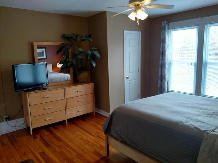 Основна спалня с вентилатор на тавана, телевизор, килер, сандък и завеси за затъмняване на стаята.