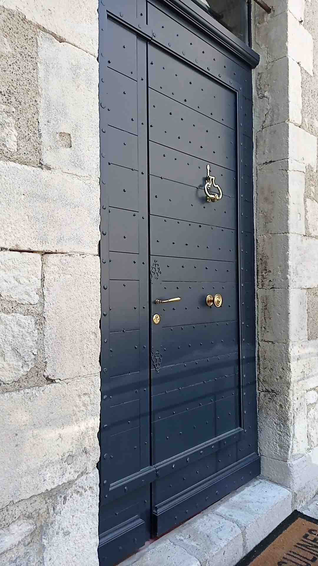 A richly detailed entrance door is presented, featuring a dark finish with a textured surface. The door is adorned with decorative brass hardware, including a door handle and knocker, while its robust, stone frame reflects the property's historical charm.