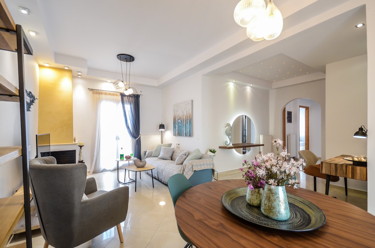 A spacious living area is presented with modern furnishings, including a comfortable seating arrangement and a dining table. Natural light filters through large windows, while an accent wall and decorative pieces add subtle character to the inviting space.