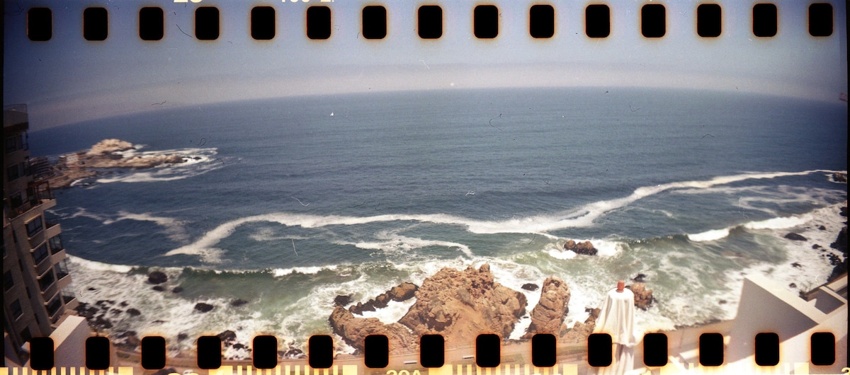 A panoramic view of the ocean is displayed, featuring rolling waves crashing against rocky shores. The calming blues of the water contrast with the earthy tones of the rocks, creating a serene coastal landscape that captures both the vastness of the sea and the beauty of nature.