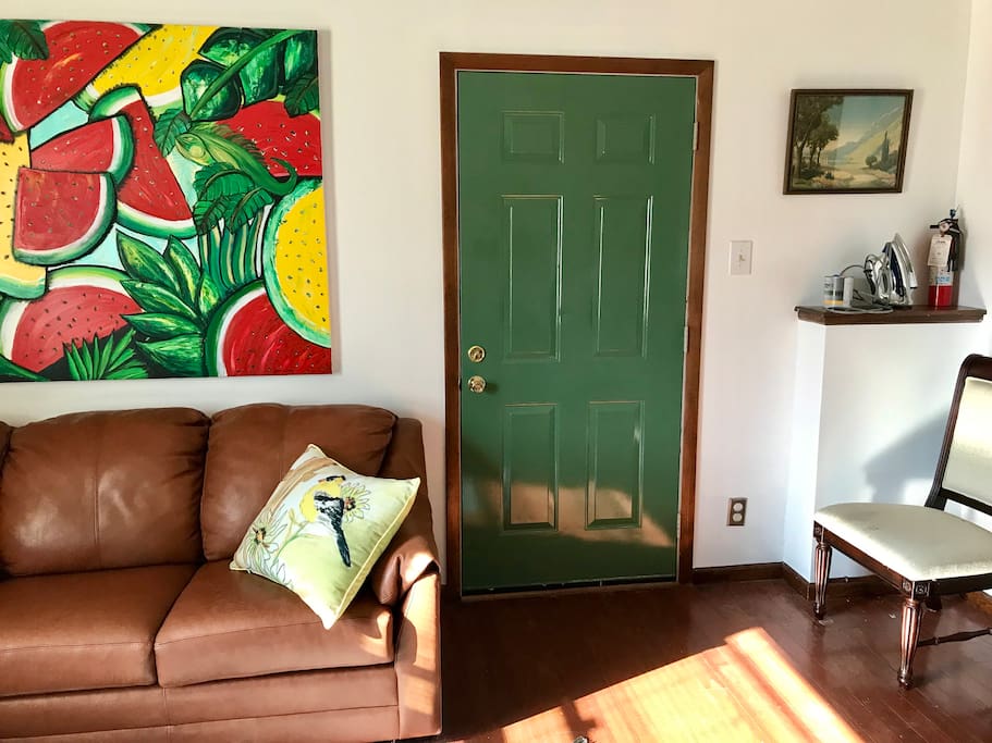 This room has a couch that makes out into a bed. It hosts the tv, and a small kitchenette. It is spacious and cozy at the same time. The green door leads to the private entrance/exit direct to a patio. Notice the iron and fire extinguisher on the ledge to the right. There is a small ironing board as well.