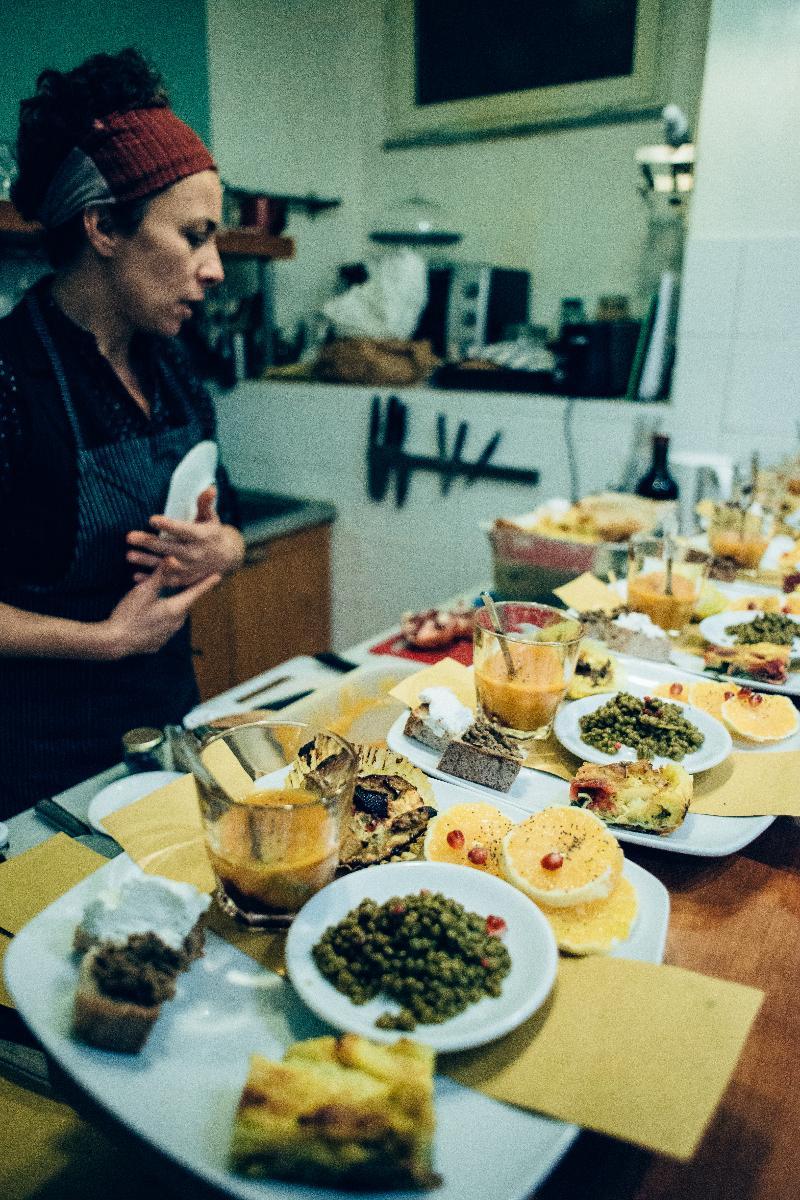 An inviting communal kitchen area showcases a display of colorful dishes on white plates, featuring fresh ingredients and a variety of meals. A carefully arranged spread indicates an emphasis on flavor and presentation, with utensils and cooking tools visible in the background.
