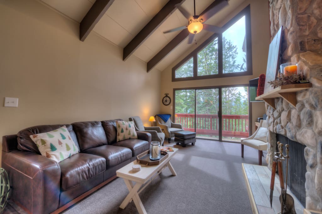 A light-filled living room has vaulted ceilings and a stone fireplace.