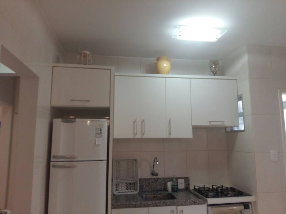 cozinha completa com cooktop, geladeira, forno microondas, forno elétrico , louças e panelas.