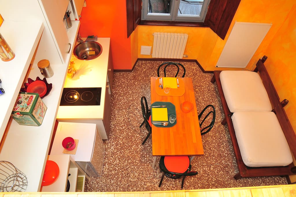 Modern kitchen with induction cooker, table with four seats, two-seater sofa and a large window overlooking the courtyard.