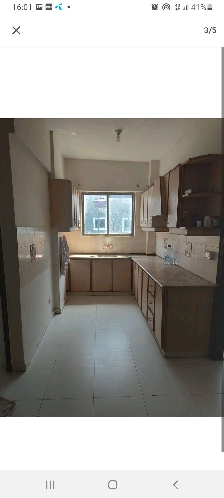 A spacious kitchen is presented with wooden cabinetry and a large window allowing natural light. Countertops are lined with essential amenities, while ample storage spaces are available in cupboards. The layout offers a practical setting for meal preparation and dining.