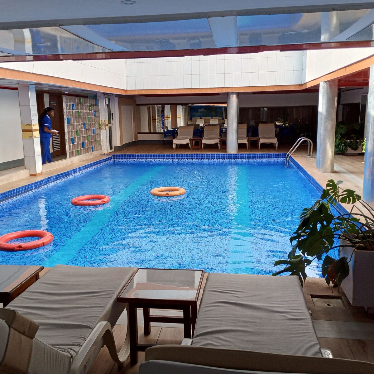 An indoor swimming pool area is visible, featuring a large, inviting pool with brightly colored flotation devices floating on the surface. Comfortable lounge chairs are arranged along the poolside, providing a place to relax. Natural light floods the space, enhancing the tranquil atmosphere.