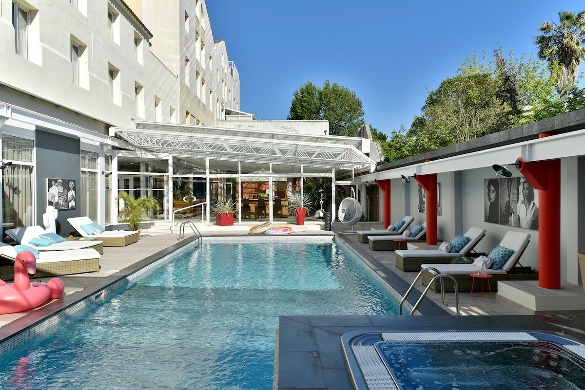 A well-maintained outdoor area features a large, heated swimming pool surrounded by lounging chairs and cushions. Bright umbrellas provide shade. A hot tub is positioned nearby, and a covered seating area is visible, fostering a relaxed environment for guests.