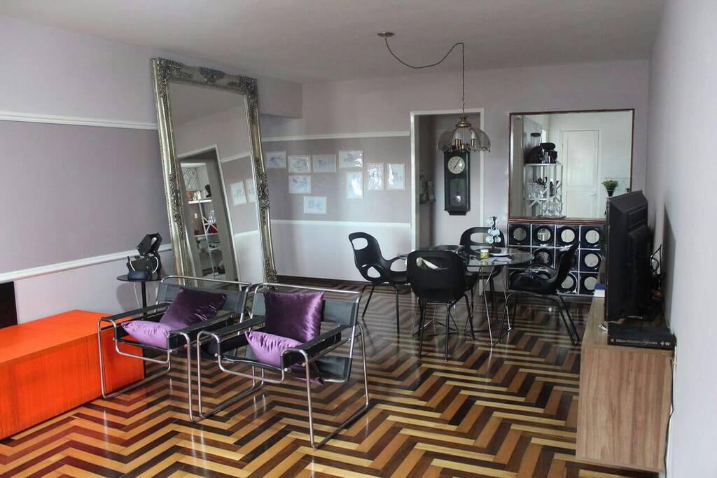 Sala ampla com sofá em "L", poltronas e mesa de jantar para 6 lugares.