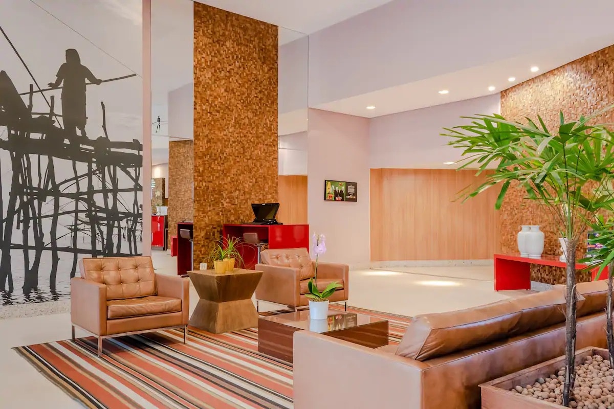 The welcoming lobby is characterized by contemporary seating arrangements, including brown leather chairs and a low table. A decorative plant adds a touch of greenery, while a large wall mural enhances the space's modern aesthetic.