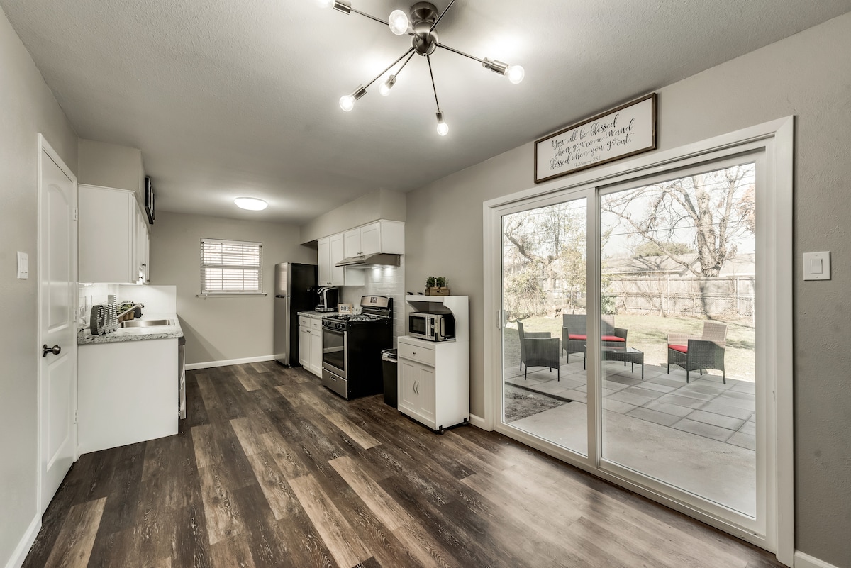 A bright kitchen area features modern appliances, including a stove and microwave. A dining space is present near large sliding glass doors, which open to the outdoor patio. Natural light fills the room, highlighting the wood-like flooring and inviting layout.