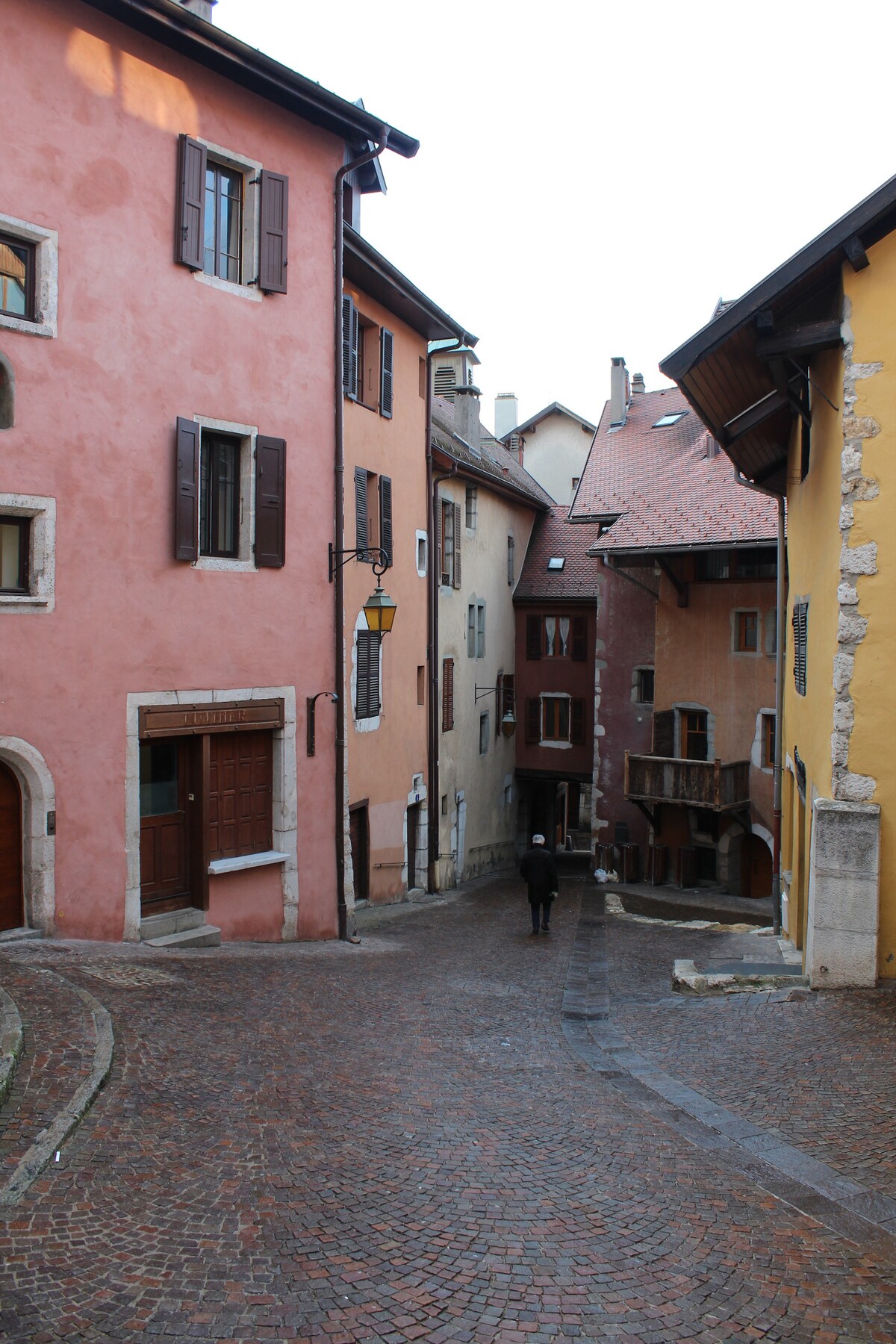 Charming streets lined with colorful buildings create a warm atmosphere in the historic district of Annecy. The cobblestone path gently winds through the narrow alley, showcasing a blend of architectural styles and inviting passerby to explore the quaint environment.