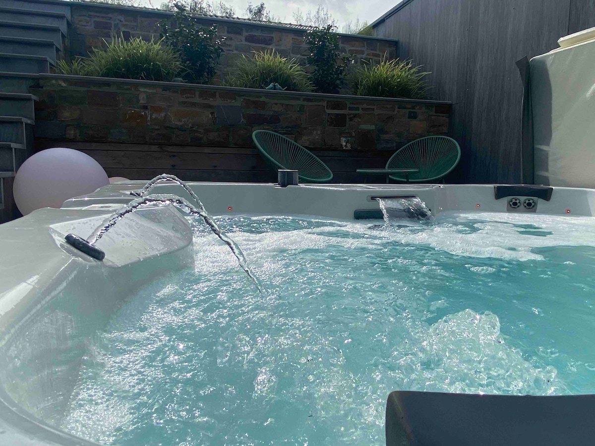 A private outdoor jacuzzi is nestled within a serene patio area. The water is heated, creating gentle bubbles and a calming ambiance. Greenery lines the background, adding a touch of nature, while a soft light illuminates the space, inviting relaxation.