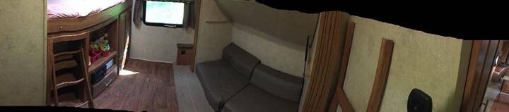 Panoramic of the back bedroom, the cushions on the ground lay out to form a larger than queen bed and there is a single bunk above, and a full on the left above the storage