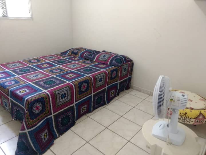 Habitación doble, que contiene ventilador, cama, sábanas, sábanas, y un pequeño armario 