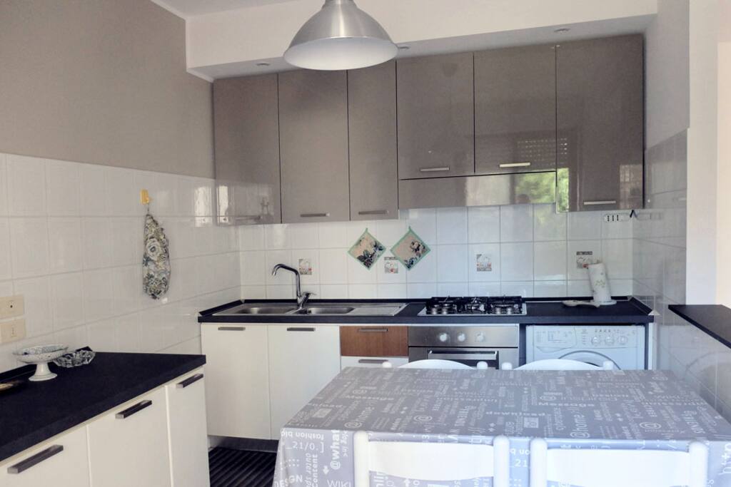 Cucina, con fornelli, lavatrice e stoviglie. Tavolo per 5 persone.