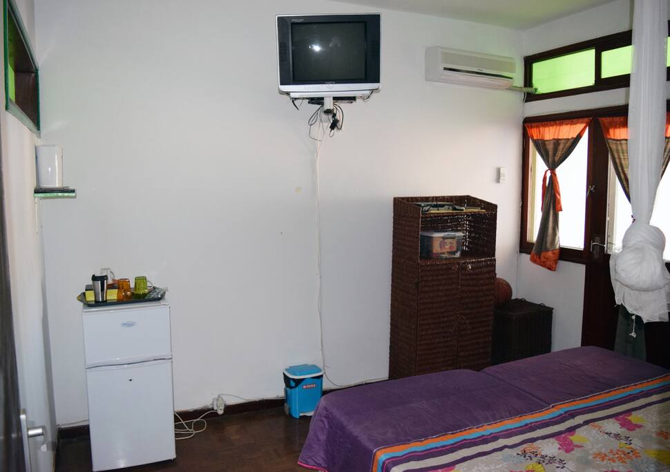 Vista do quarto a partir da porta de entrada. Frigorífico, facilidades de chá/café, TV e ar condicionado visíveis