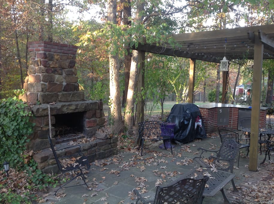 lighted outdoor kitchen area with grill, fireplace, and fridge