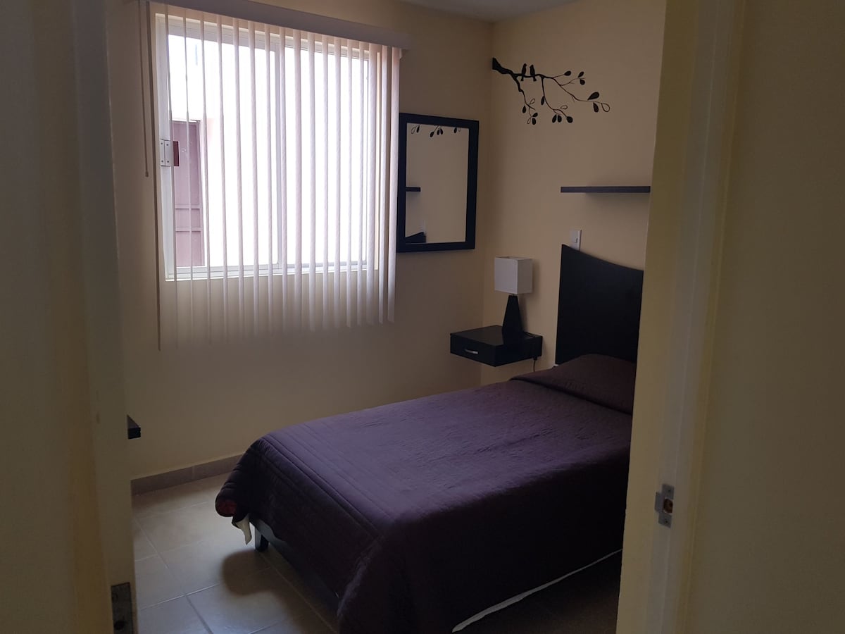 Recámara con cama individual, escritorio y guarda ropa.