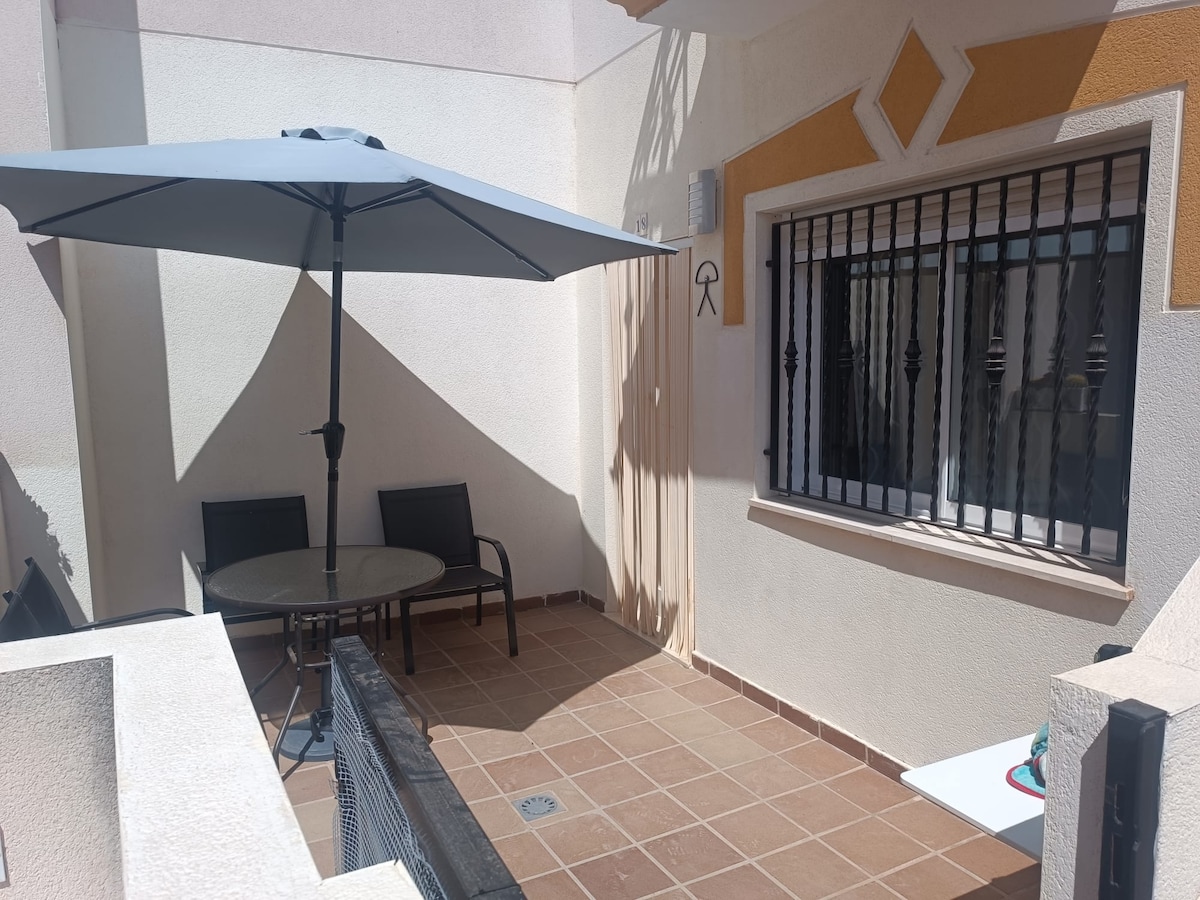 A private outdoor area is presented, featuring a round table with two chairs beneath a large umbrella. The tiled floor and surrounding walls create a serene space. A window, equipped with decorative grilles, allows light to enter while maintaining privacy.