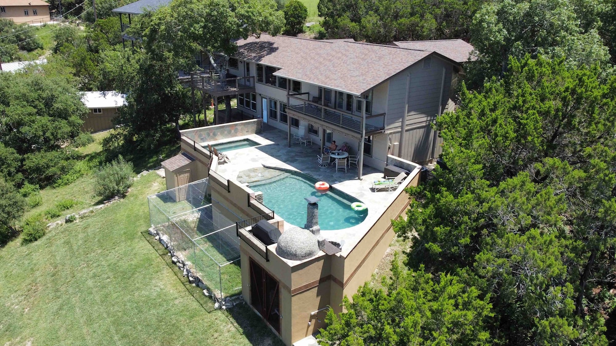 An aerial view captures the two-story home surrounded by lush greenery. A private pool and spa are visible in the backyard, bordered by a spacious patio. Lounge chairs sit invitingly beside the pool, while a deck extends from the upper level, enhancing the outdoor living space.