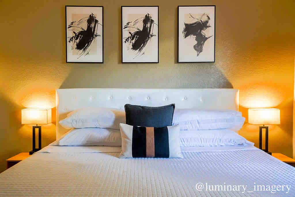 A comfortable king-sized bed is presented, featuring a plush headboard and neatly arranged linens. Two bedside lamps cast a warm glow, and framed artworks are displayed above the bed, adding a touch of elegance to the serene environment.