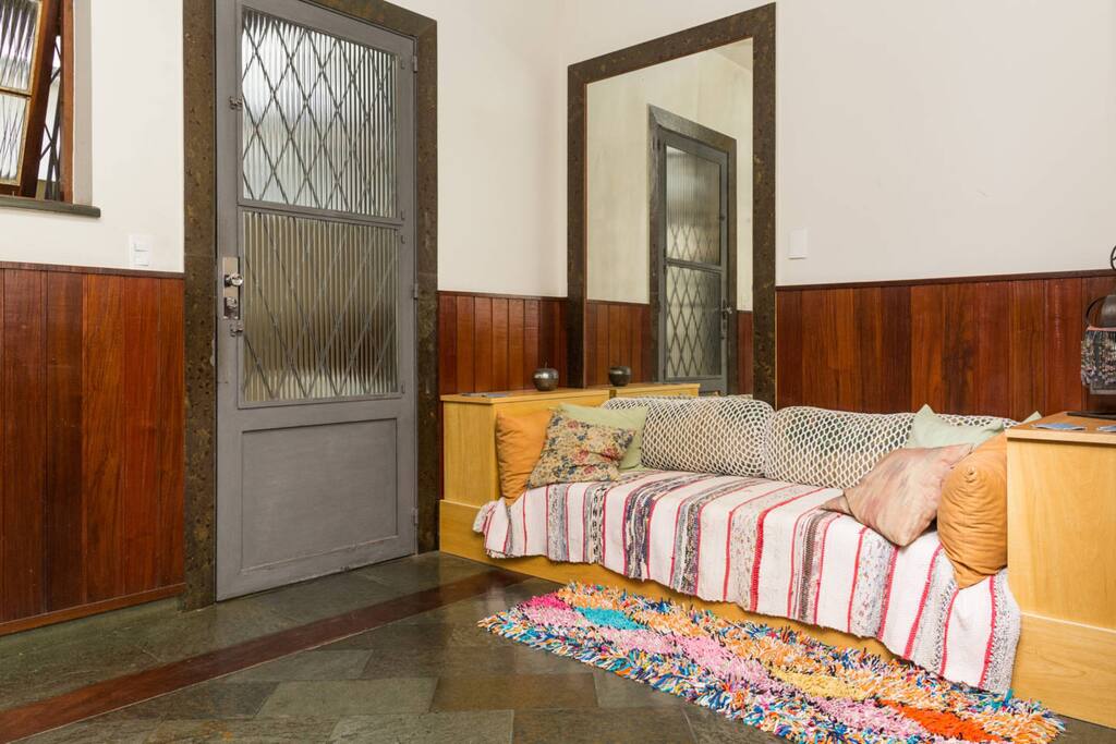 Sala de estar sofá, porta de entrada fechada, janela para manter a ventilação.