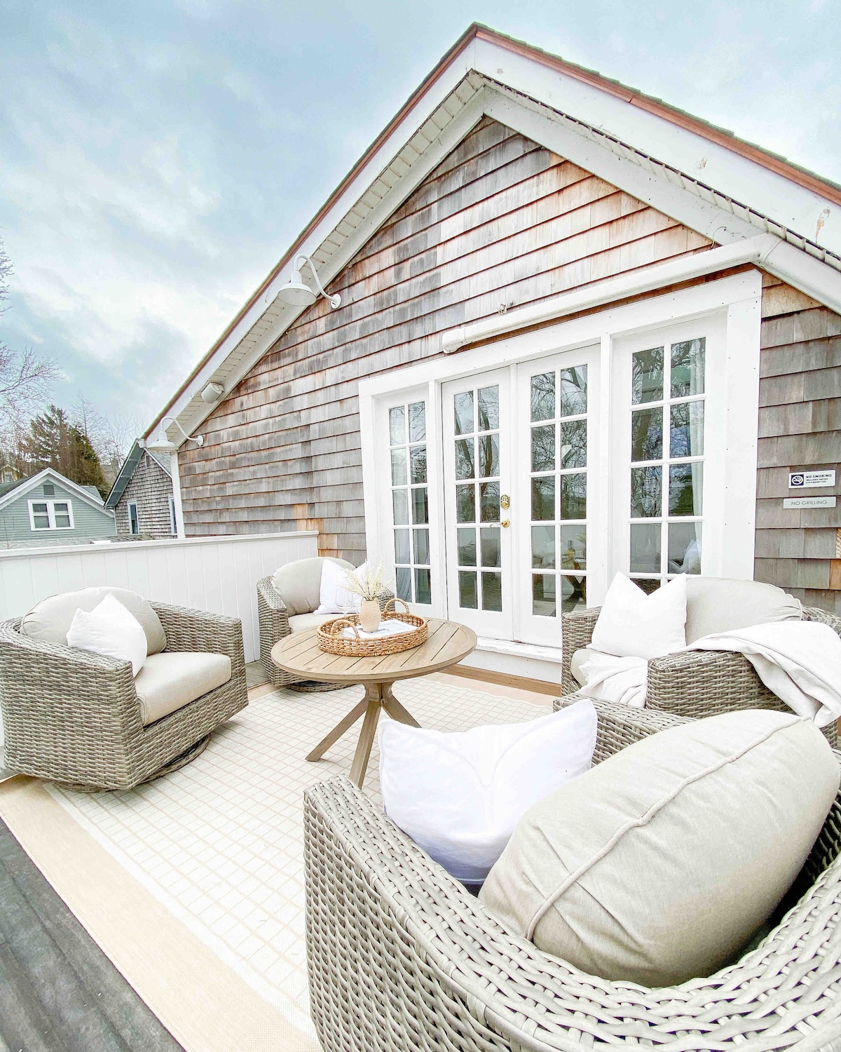 A private deck is furnished with two wicker chairs and a small round table, featuring soft cushions for comfort. The deck is surrounded by wooden shingles and offers a peaceful space for relaxation, with sliding glass doors providing indoor access.