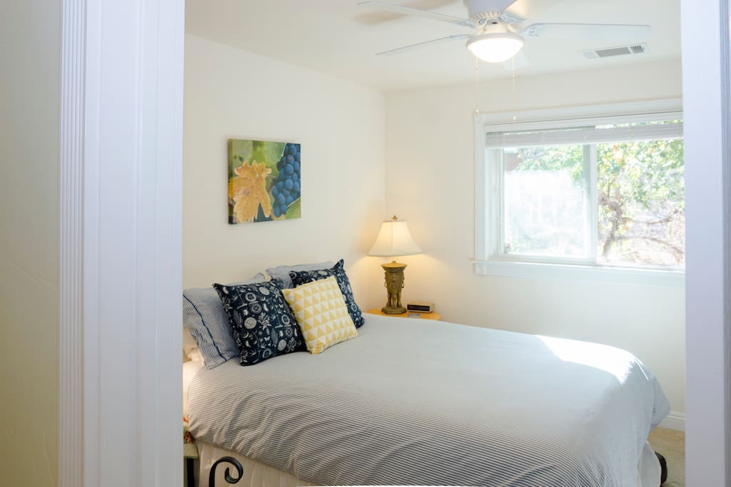 Comfortable queen sized bed with ceiling fan, window and large closet.