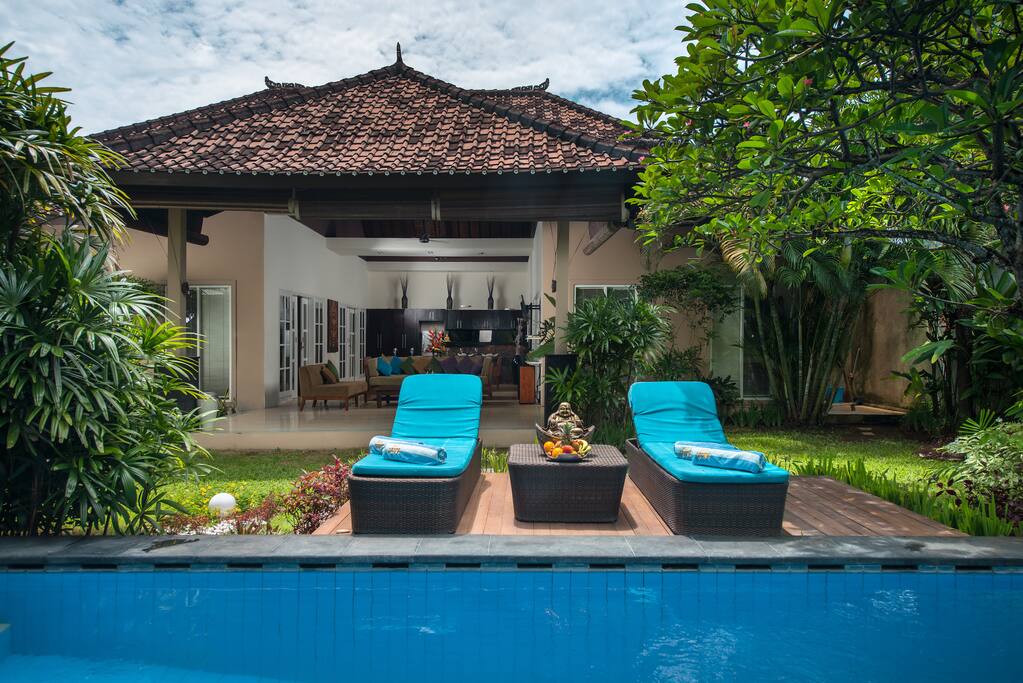 Crystal clean swimming pool with sunbeds surrounded by tropical tries and plants