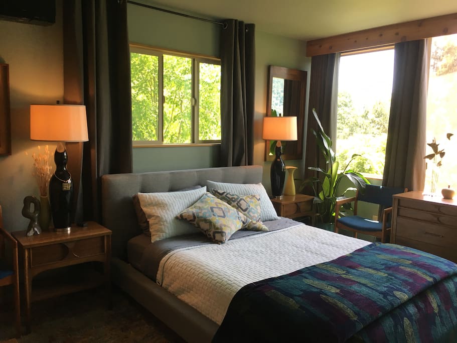 Comfortable queen bed in master bedroom with bank of windows overlooking the view.