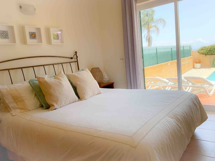 Principal bedroom with queen sized bed, and access to pool side lounging area. Ocean views from bedroom are visible.