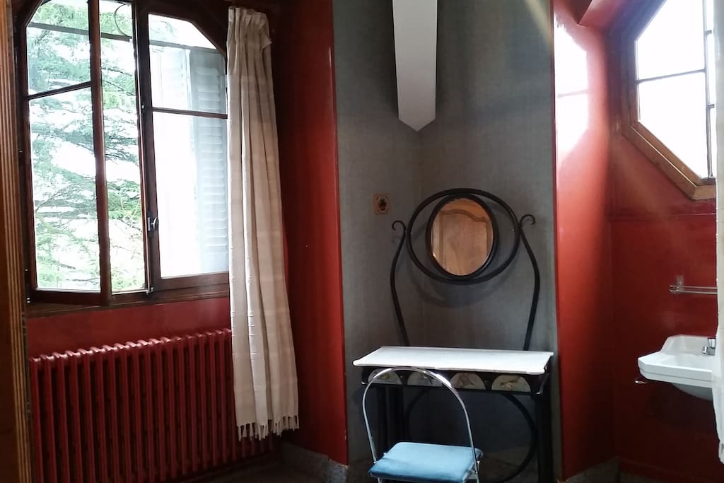 Chambre à coucher avec 2 fenêtres, une donnant vue sur parc arboré et la 2è exagonale donnant sur la rue privée, lavabo, table de maquillage, armoire de rangements.