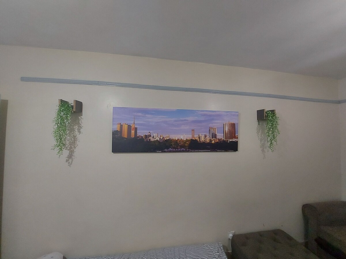 A wall display features a panoramic cityscape photograph, complemented by two small wall-mounted plant holders displaying green foliage. The setting is enhanced by a neutral wall color, providing a contemporary backdrop for the artistic elements.