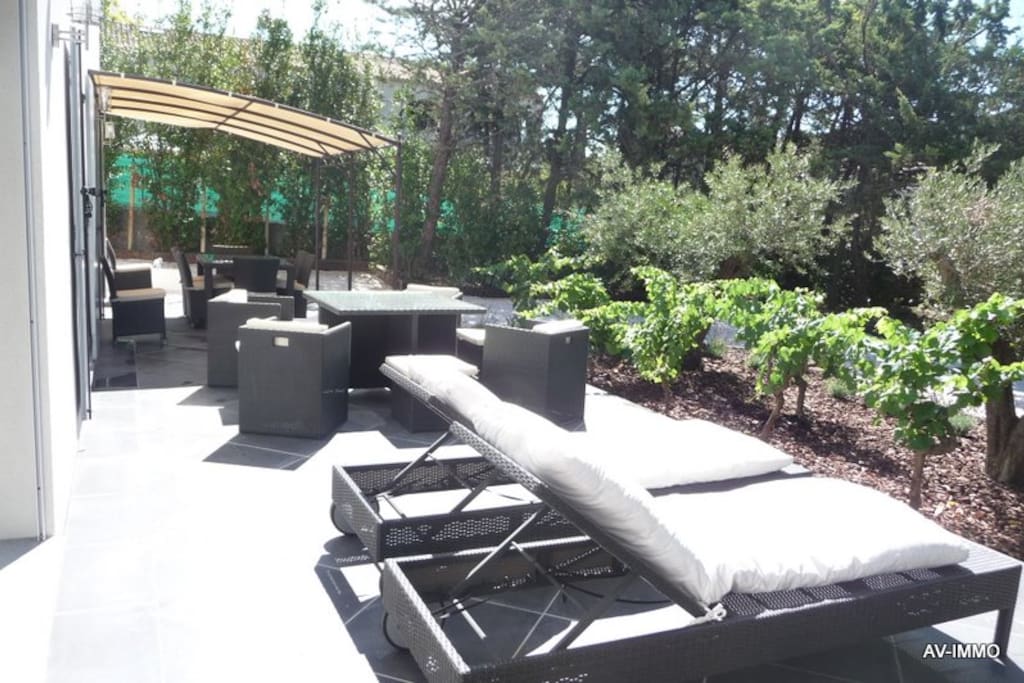 terrasse avec table pour 8 personnes , salon de jardin et 4 chaises longues.