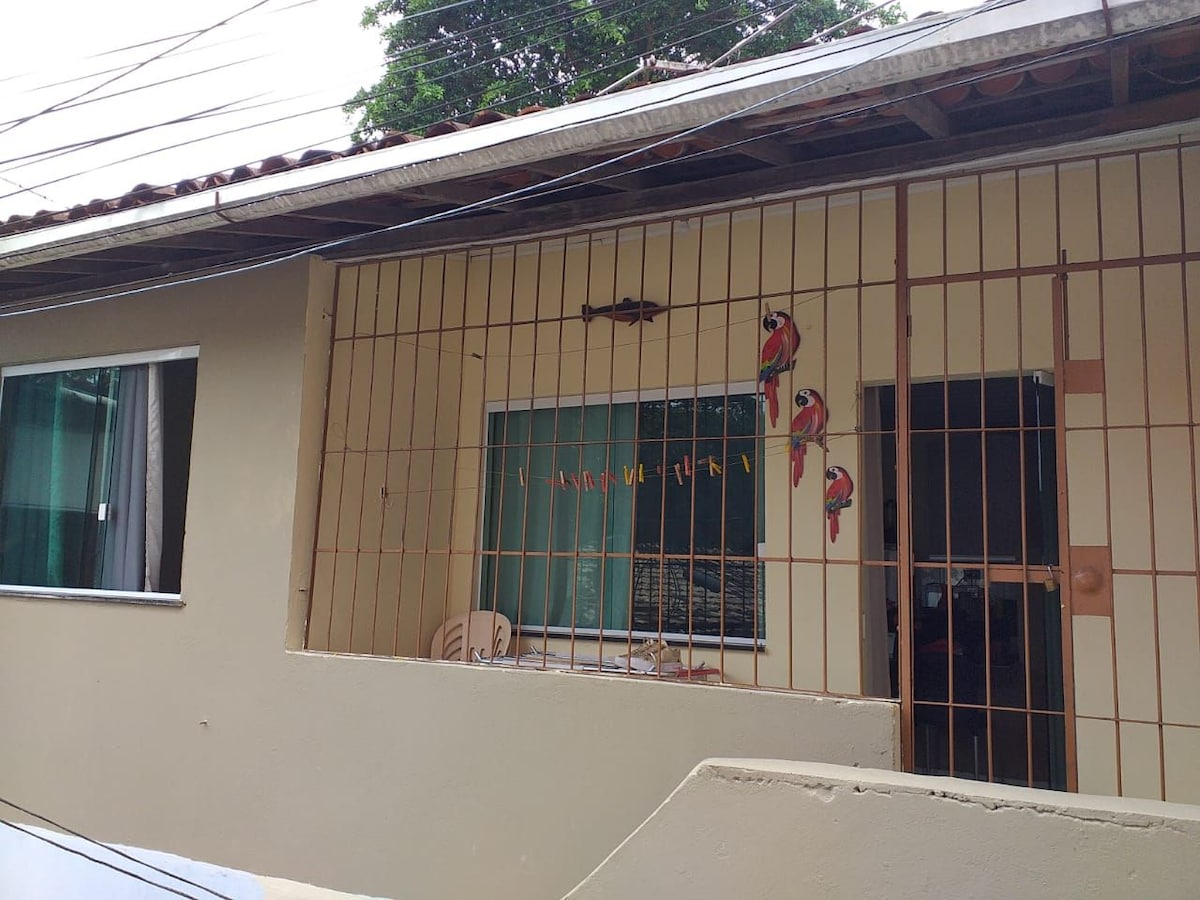 A well-designed exterior features a sturdy barred window, allowing natural light to fill the interior. Colorful parrot decorations are placed above the window, enhancing the cheerful ambiance. Surrounding greenery complements the home's inviting presence, while a portion of the nearby outdoor area is visible.