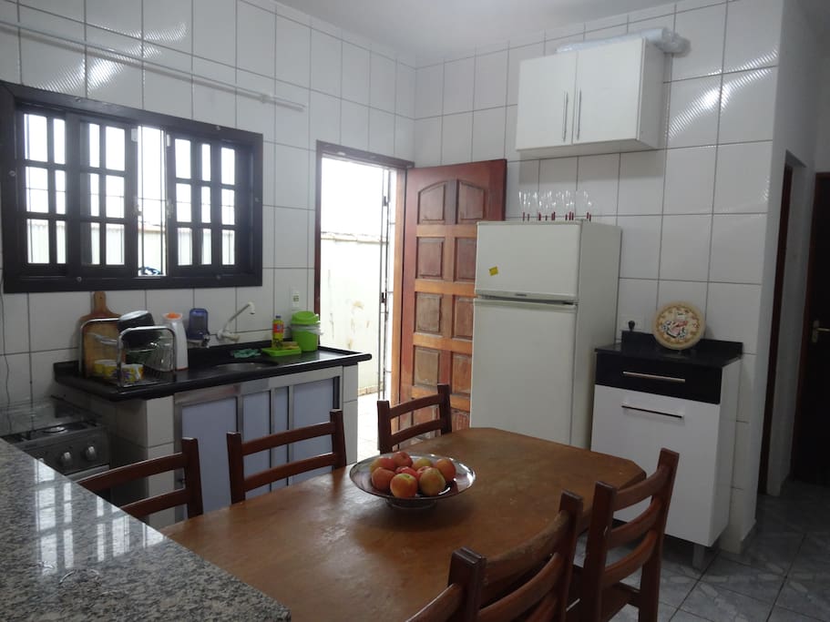 Cozinha completa e equipada com fogão e forno, microondas, geladeira, pia, armários, utensílios de cozinha e mesa com 6 cadeiras.