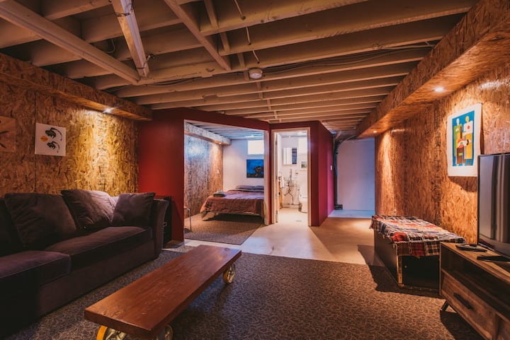 Basement area with full size bed next to two-piece bath and tv/family room with pull out sofa.