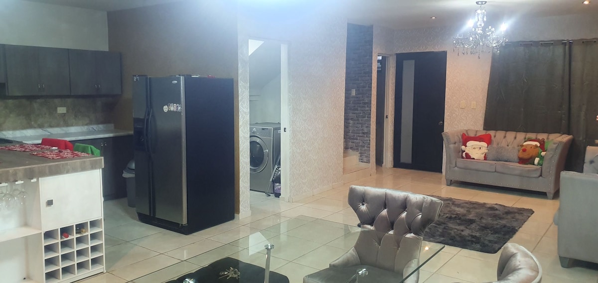 The open living area showcases a modern kitchen with dark cabinets and a large black refrigerator. A plush gray sofa offers comfortable seating, while a stylish coffee table sits atop a soft area rug. Natural light enters through glass doors leading to another space.