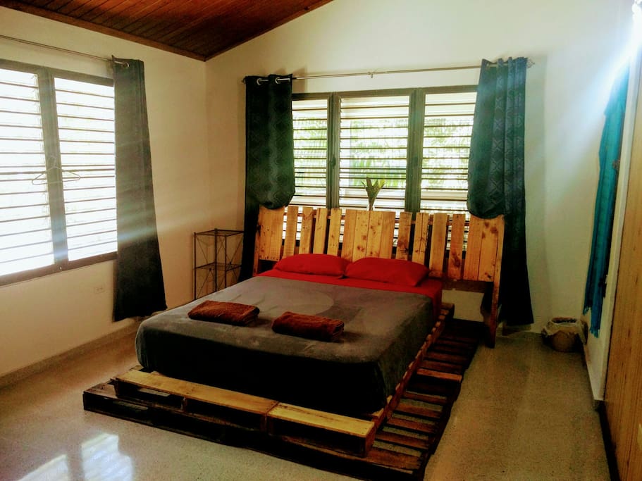 Bright room with high ceiling, queen bed and homemade bed frame with pallets