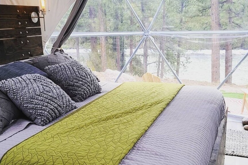 A comfortable sleeping area is highlighted by a spacious bed adorned with textured pillows and a green quilt. Large windows frame the serene view of the outdoors, allowing natural light to enhance the inviting atmosphere.