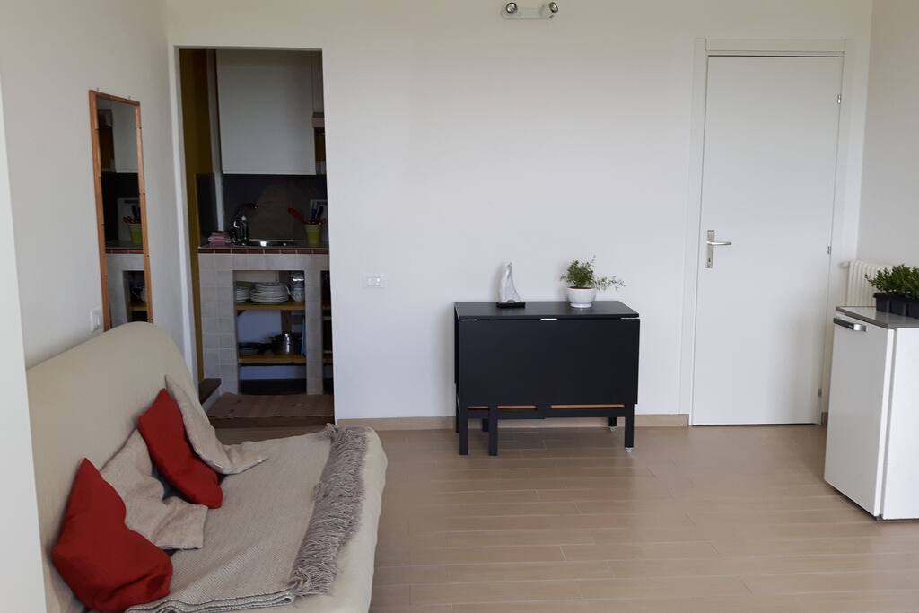 Il divano letto, il tavolo pieghevole da 6 persone e il cucinotto. La porta bianca è l'ingresso del bagno