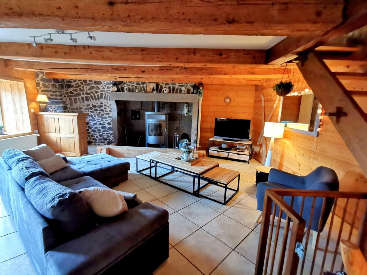 An open living area features a cozy seating arrangement with a large sofa and wooden coffee table. A stone fireplace serves as a focal point, complemented by a flat-screen television on an understated stand. Natural light illuminates the warm wooden walls and tiled flooring.