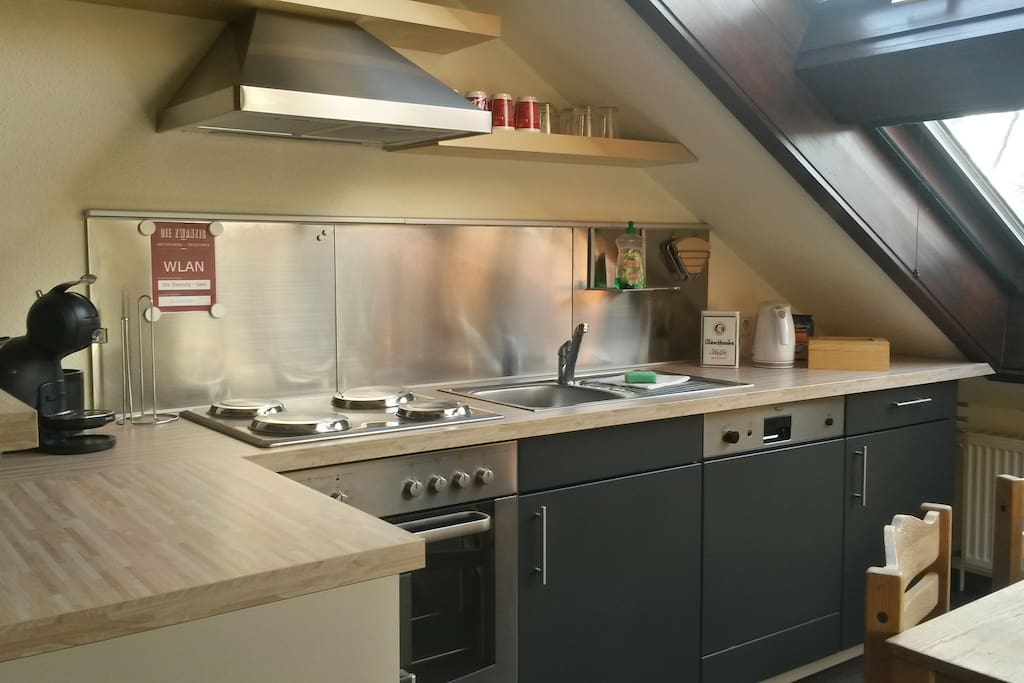Eine voll ausgestattete Wohnküche mit Esstisch und Bar, Herd, Kühlschrank, Spülmaschine, Wasserkocher, Kaffeemaschine, Toaster und Geschirr.