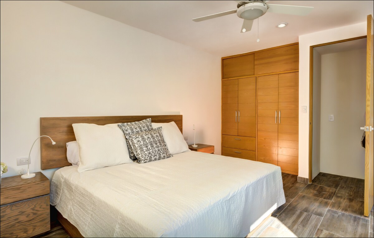 Druhá spálňa s manželskou posteľou King.  Na okne sú teraz zatemnené záclony a na stene televízor s plochou obrazovkou.