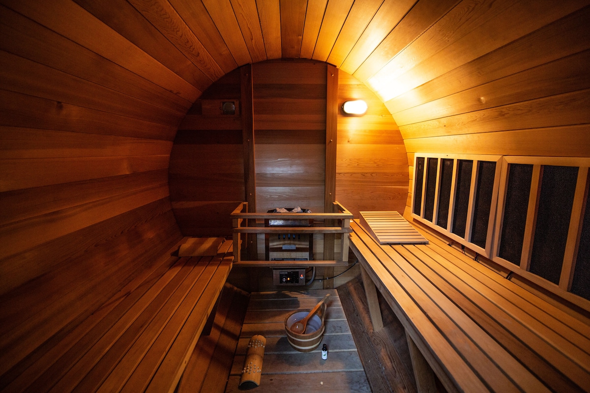 An infrared sauna is showcased, featuring smooth wooden benches along the curved walls. Soft lighting creates a warm ambiance, highlighting the cedar wood's natural tones. A small shelf for personal items is visible, and a heater is placed unobtrusively for warmth.